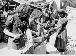 Rubble women chipping cement off of bricks